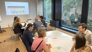 Mehrere Personen sitzen an einem Tisch und tauschen sich aus.
