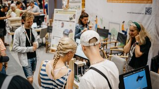 Besuchende an Messestand der KI-Ideenwerkstatt testen Ausstellungsstücke