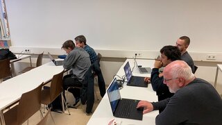 An zwei langen Tischen sitzen Personen vor Laptops.