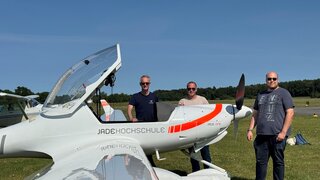 Vor einem Leichtflugzeug stehen drei Männer