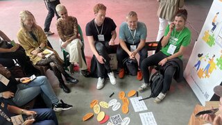 Teilnehmende sitzen im Kreis, auf dem Boden liegen farbige Zettel.