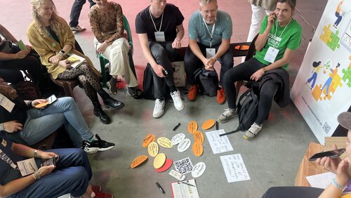 Teilnehmende sitzen im Kreis, auf dem Boden liegen farbige Zettel.