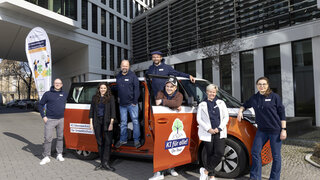 Das Team der KI IW steht vor dem orangenen E Bus. Daneben steht die Flagge der KI IW