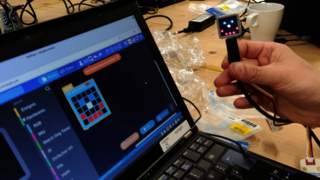 Zu sehen ist ein Laptop, eine Hand hält ein an das Laptop angeschlossenes Messgerät hoch.