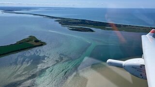 Blick von oben aus dem Flugzeug auf das Meer und eine langgezogene Insel.