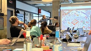 Teilnehmende schauen auf Leinwand, worauf Animation eines vollen Hauses zu sehen ist