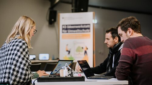 Gruppe Teilnehmender arbeitet mit ihren Laptops an einem Gruppentisch