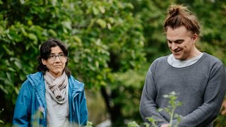 Eine Frau und ein Mann stehen vor einem Beet, im Hintergrund Bäume