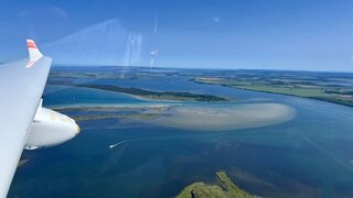 Blick von oben aus dem Flugzeug: Zu sehen ist ein Teil der Tragläche, das Meer sowie die Insel Rügen.