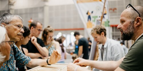 Zwei Personen unterhalten sich, im Hintergrund ein Messestand der KI-Ideenwerkstatt
