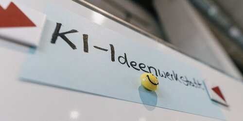 Auf einer Flipchart ist eine Karteikarte mit der Aufschrift "KI-Ideenwerkstatt" gepinnt