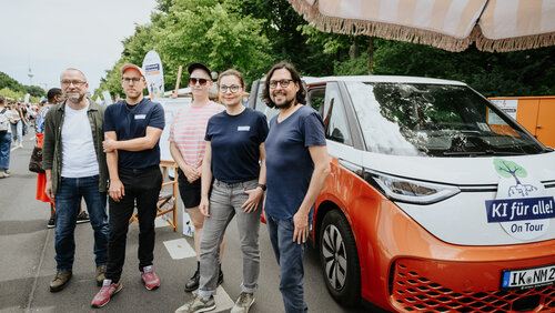 Das Team der KI Ideenwerkstatt steht vor dem orangenen Bus mit der Aufschrift KI für alle on Tour