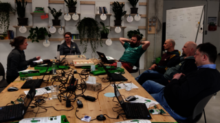 Mehrere Personen sitzen um einem großen Tisch mit vielen Laptops und Sensorikgeräten